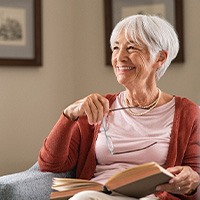 Woman with glasses smiling while reading book at home