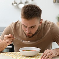 A young, bearded man eating soup in a kitchen