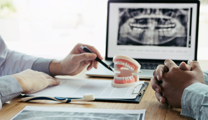 Dentist’s and patient’s hands at desk going over model teeth, X-ray, and treatment plan