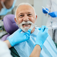 Man with white hair in purple dental chair about to undergo exam