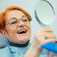 Woman with orange hair and glasses in dental chair smiling into mirror