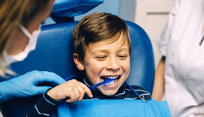 little boy brushing teeth in dental chair 