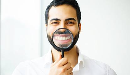 man using magnifying glass to display his smile with dental crowns in St. Albans 
