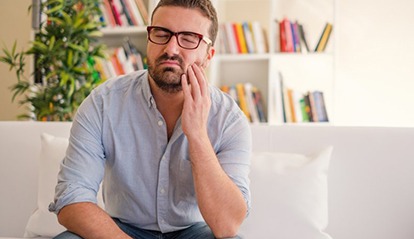 man sitting on couch and holding his mouth in pain 