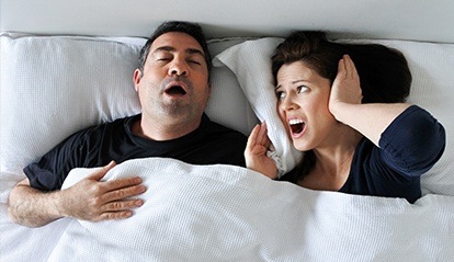 Woman covering ears next to snoring man