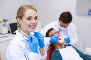 Dental hygienist smiling into the camera as the dentist works on a patient’s teeth