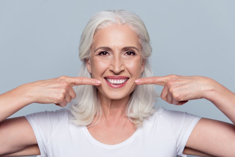 Older woman smiling with teeth and pointing fingers on each sides of her mouth