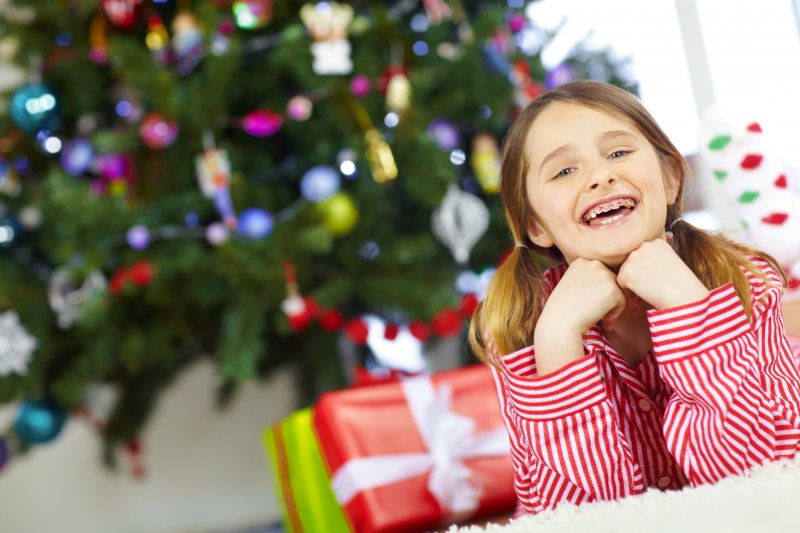 A child smiling under their holiday tree after a smile-friendly gifts exchange