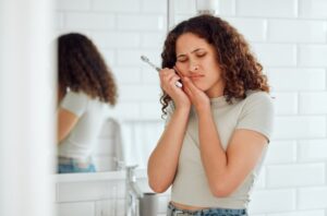 Young woman in pain brushing teeth.