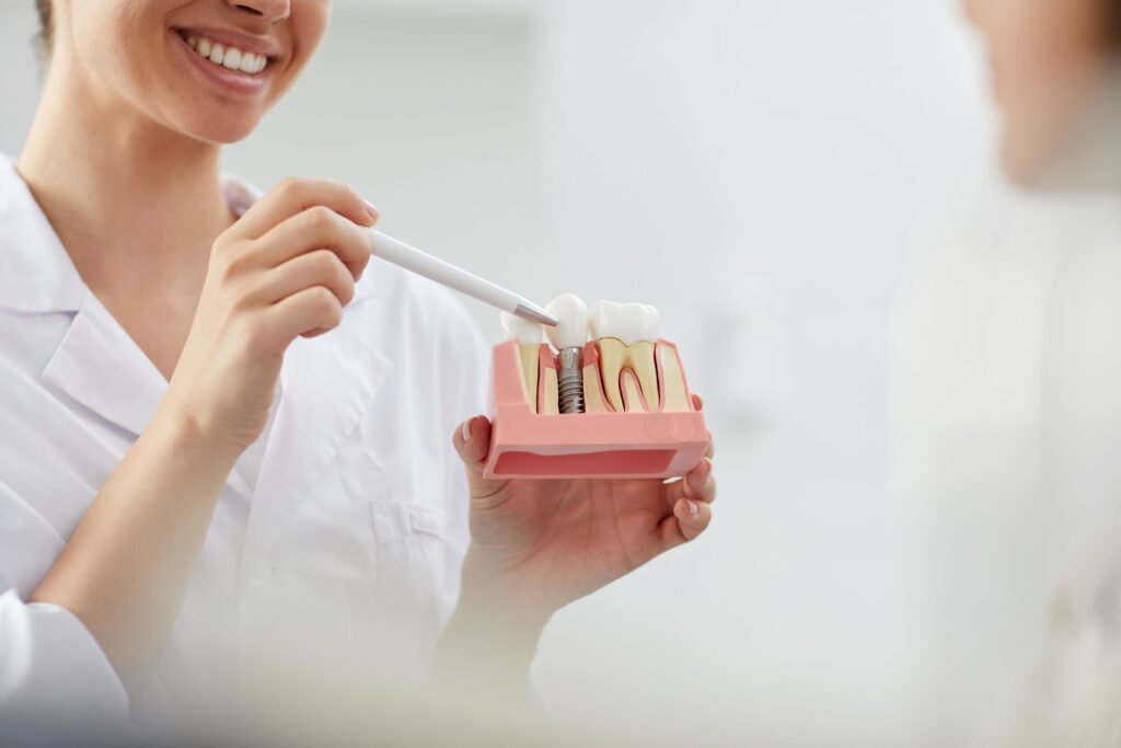 Dentist wearing white pointing to sample dental implant